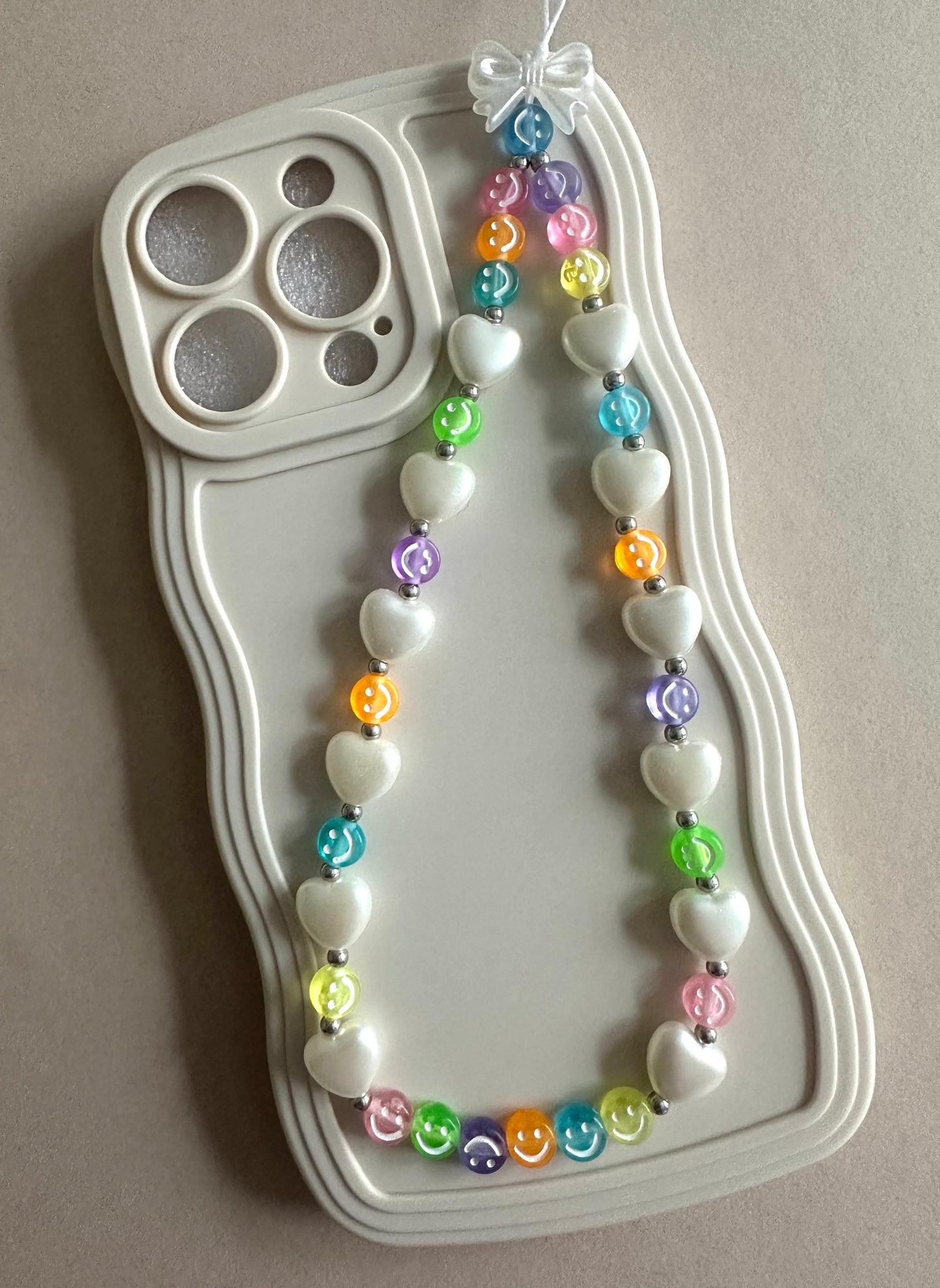 Colorful handmade phone charm with beads and heart-shaped pendant attached to white phone case