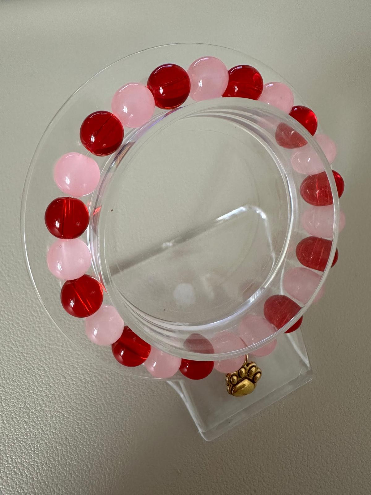 Golden furry friend stretch bracelet with red and pink beads and golden paw charm