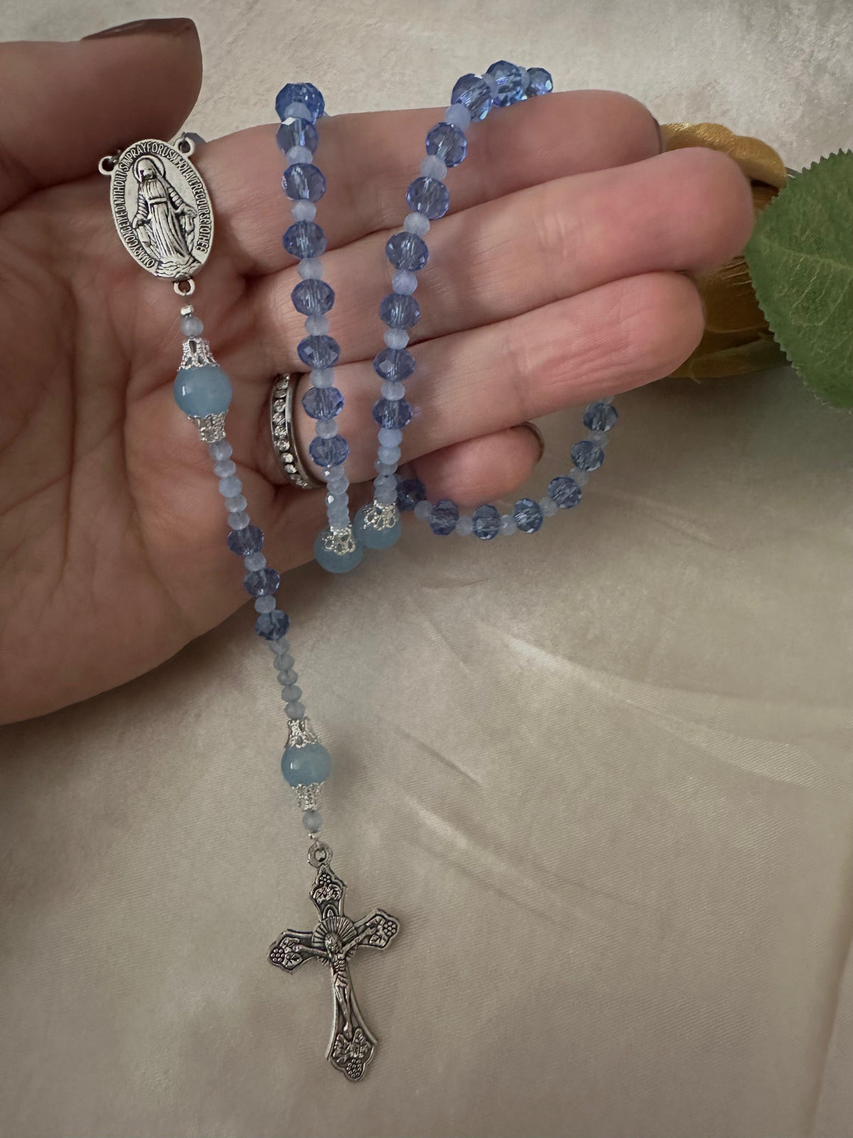 Blue Serenity Handmade Rosary with translucent blue glass beads, silver-tone filigree details, Virgin Mary centerpiece and crucifix.