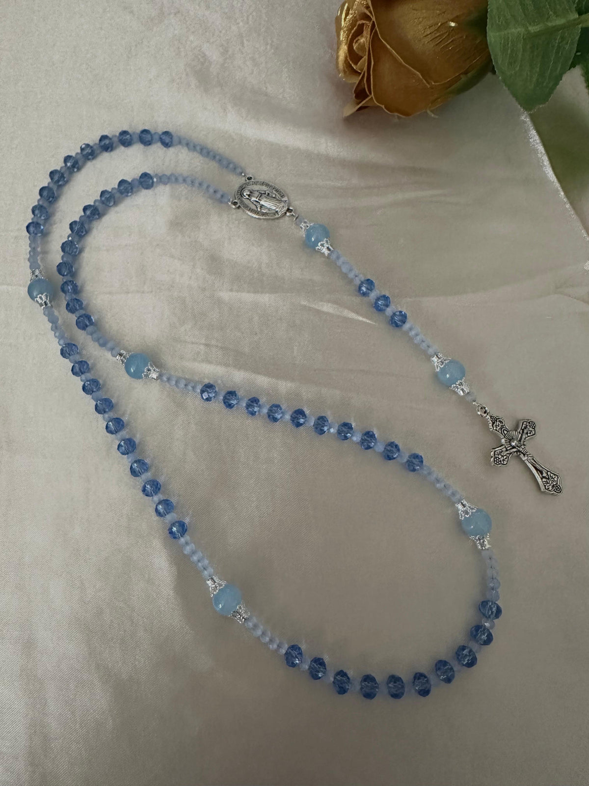 Blue Serenity Handmade Rosary with blue and light blue glass beads, silver-tone filigree caps, Virgin Mary centerpiece and crucifix.
